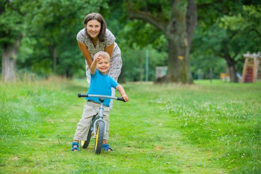 Portrait of little boy on a bicycle and his mother in the summer park