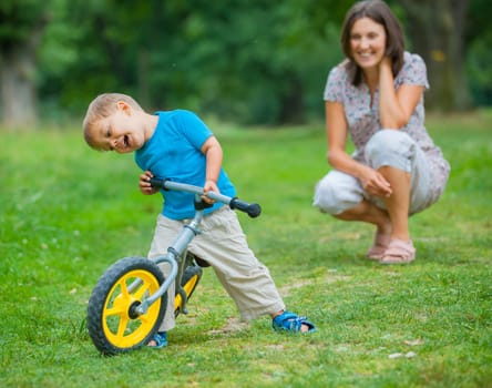 Portrait of little boy on a bicycle and his mother in the summer park