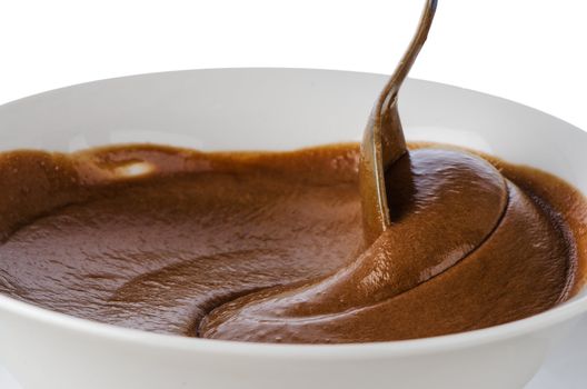 Chocolate mousse on a white mug with spoon on white background.