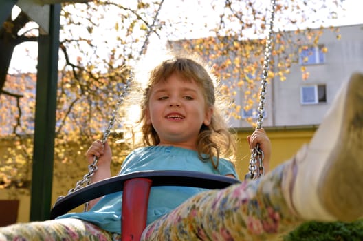 Photo shows a little girl on a swing at the playground in the park.