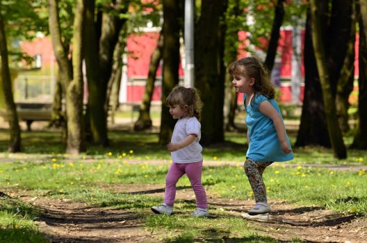 The picture shows two sisters, the elder takes care of the younger at the time having fun in the park.