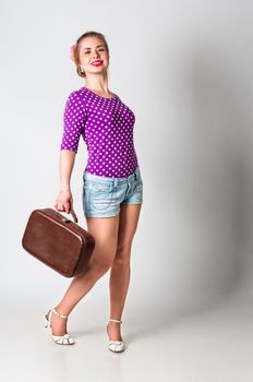 Pin up girl standing with bag for travelling, studio shot