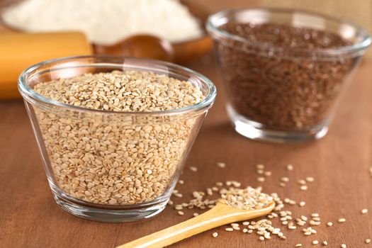 Sesame seeds in glass bowl with flax seeds and flour in the back (Selective Focus, Focus one third into the sesame seeds in the bowl)