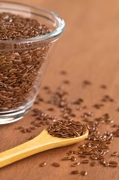 Brown flax seeds on wooden spoon with glass bowl on the side (Selective Focus, Focus on the front flax seeds on the spoon)