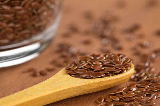 Brown flax seeds on wooden spoon with glass bowl on the side (Selective Focus, Focus on the front flax seeds on the spoon)