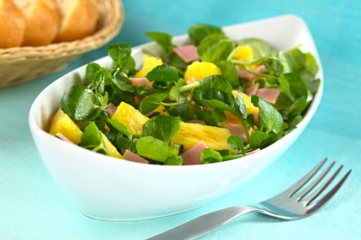 Fresh watercress, pineapple and ham salad in elongate white bowl with baguette slices in the back (Selective Focus, Focus on the two pineapple pieces one third into the salad)