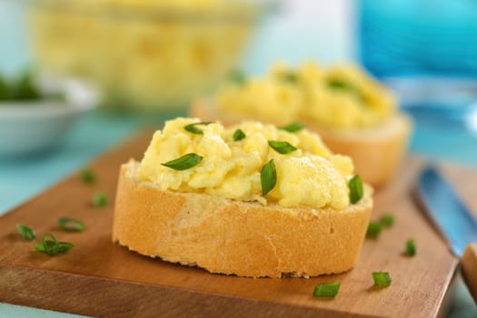 Scrambled eggs on baguette slices with green onion on wooden board (Selective Focus, Focus on the front of the first sandwich) 