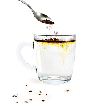 Granulated Coffee poured from a spoon into a glass mug with hot water, a few grains of coffee on the desk isolated on white background
