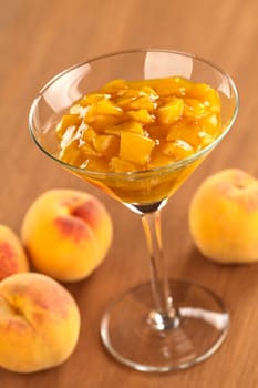 Fresh peach compote in cocktail glass on wood (Selective Focus, Focus one third into the glass) 