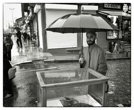 WAITING IN THE RAIN, ISTANBUL, TURKEY, APRIL 14, 2012: Simit vendor under his umbrella is waiting for customers in the rain in urban Istanbul near the Blue Mosque.