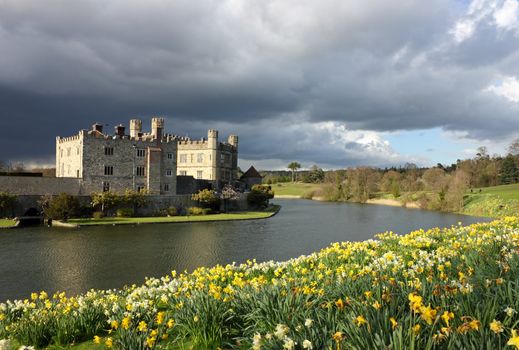 Leeds Castle in Kent, United Kingdom with blooming daffodils and dramatic sky.