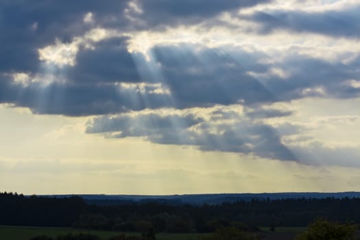 This image shows clouds with shafts of sunlight and forest