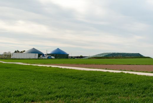 Different fermenters of a biogas plant in front of a cloudy blue sky