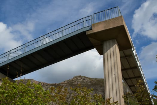 A raised walkway with a concrete supporting pillar and metal hand railings against a blue cloudy sky.