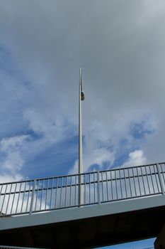 A raised walkway and metal hand railings and a street light post against a blue cloudy sky.