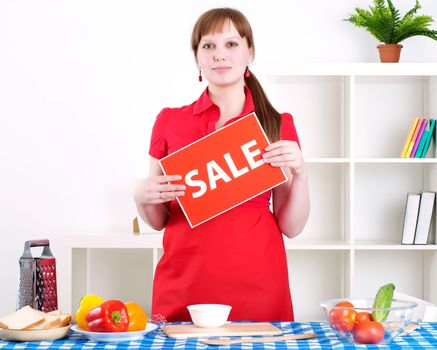 Young woman cooking fresh meal at home and holding sale sign