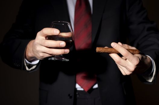 man in a business suit holds a cigar and a glass with whisky