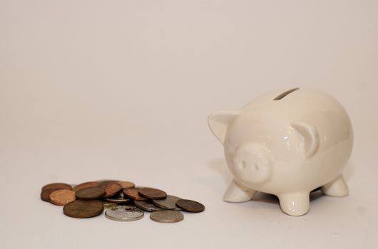 Ceramic piggy money box with it's snout in a pile of coins against white background with copy space