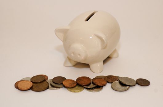 China/ ceramic piggy money box with it's snout over a pile of coins against white background with copy space