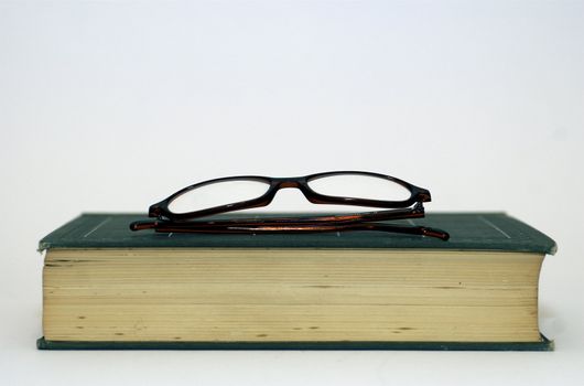 Spectacles/ glasses on top of an old book against a white background with copy space