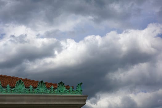 Darkening clouds over a read tile roof with green ornate decorations