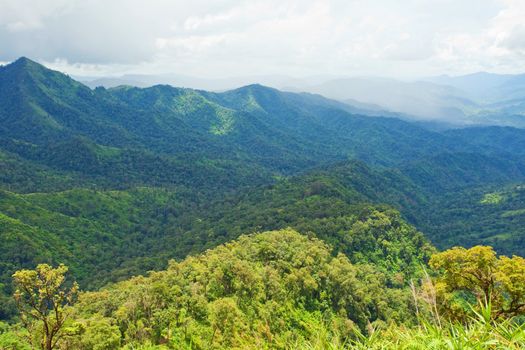 Mountain by green grass and cloudy blue sky