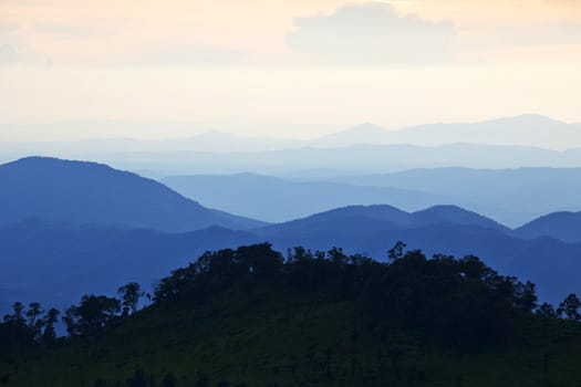 Mountain by green grass and cloudy blue sky