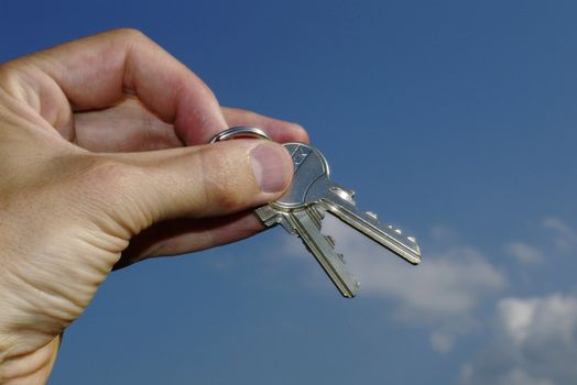 Hand holding keys against blue sky