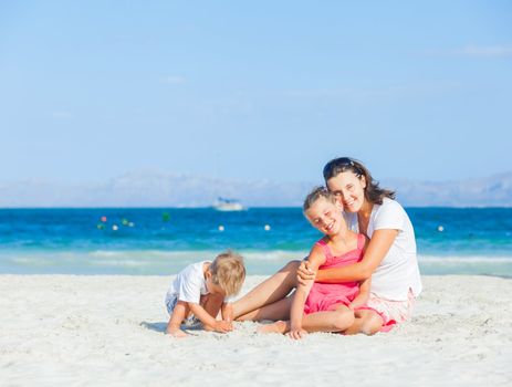 Happy family of three sitting and having fun on tropical beach