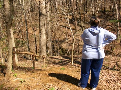 A woman standing on the edge of a ravine looking into the woods