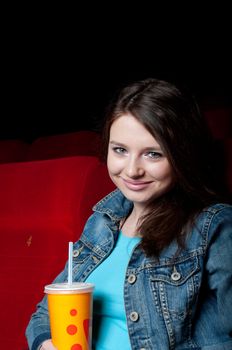 beautiful woman in a movie theater, watching a movie and drink a drink