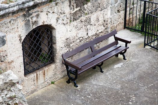 Lonely bench next to window with metal grate