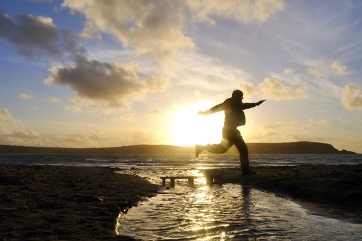 Silhouette of one man jumping over water at the beach.