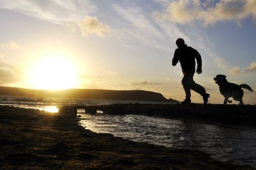 Silhouette of one man running on the beach with his dog.