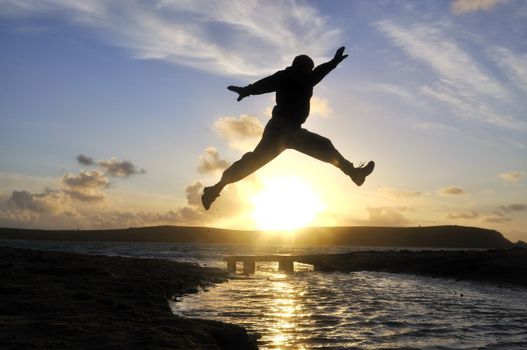 Silhouette of one man jumping over water at the beach.