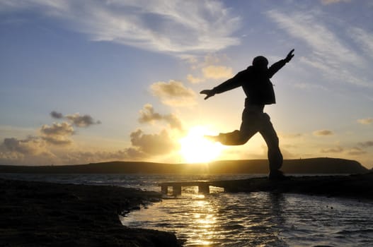 Silhouette of one man jumping over water at the beach.