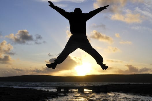 Silhouette of one man jumping over water at the beach.