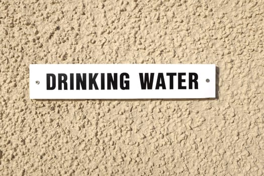 A cream coloured wall with a white sign with 'DRINKING WATER' written in black.