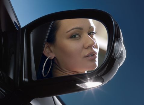 Young woman sits on driver's seat and Looks in the rear-view mirror