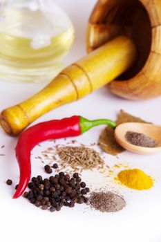 Mortar with pestle, variety of spices and oil over white