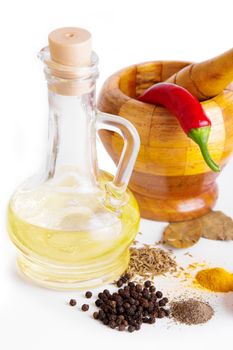 Mortar with pestle, variety of spices and oil over white