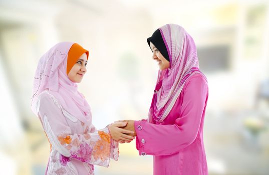 Muslim woman in traditional clothing greeting to each other, indoor.
