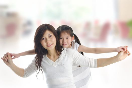 Happy Asian mother piggyback ride daughter indoor