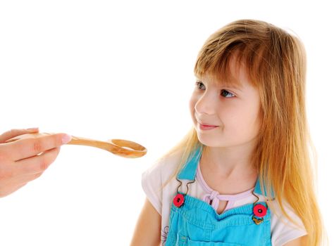 Small beauty girl is taking a white tablet in wooden spoon from female hand on white background