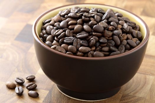 cup overflowing with dark roasted coffee beans, fresh and ready to grind