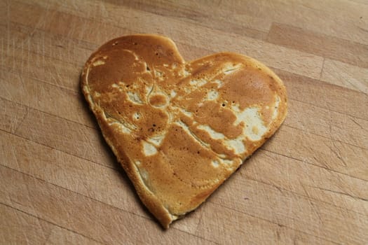A pancake shaped as a heart, on a wooden table. A sweet way to say I love you