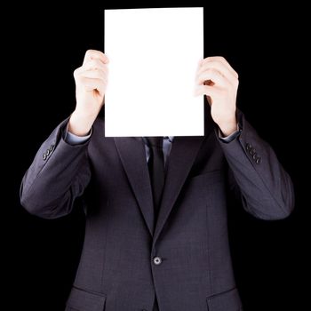 Businessman holding  a sheet of paper in front of his face isolated on black background