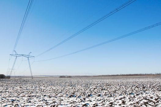 Line of electric pylons and long caples on winter snow-covered field