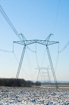 Line of electric pylons on winter snow-covered field
