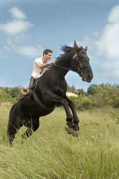 young man and his black stallion in  a field